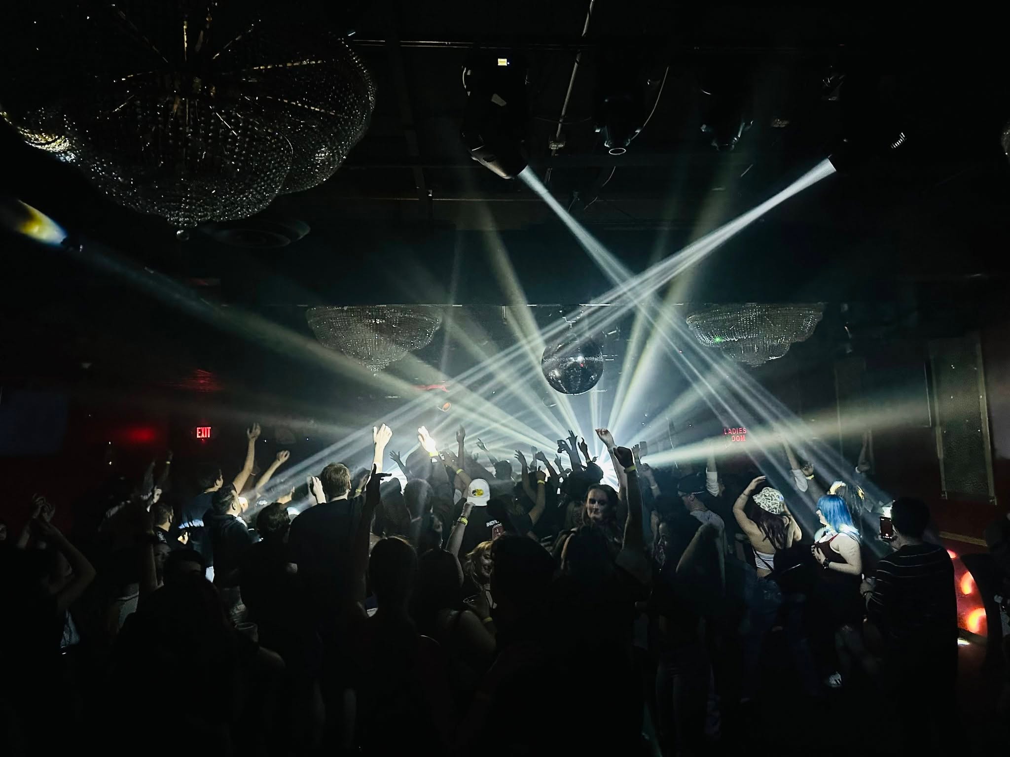 Crowd with hands raised under dramatic white beam lighting and chandeliers